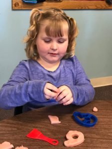 Child cutting playdoh with cookie cutters.